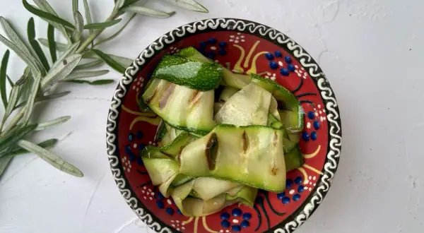Gegrillte Zucchinibänder in einer bunten Schale, daneben Rosmarin. Perfekt, um zu sehen, was passt zu Zucchini!