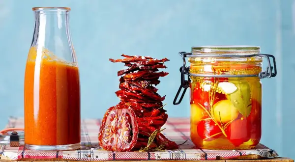 Glas mit eingelegten Tomaten, daneben ein Stapel sonnengetrockneter Tomaten und eine Flasche Tomatensauce.