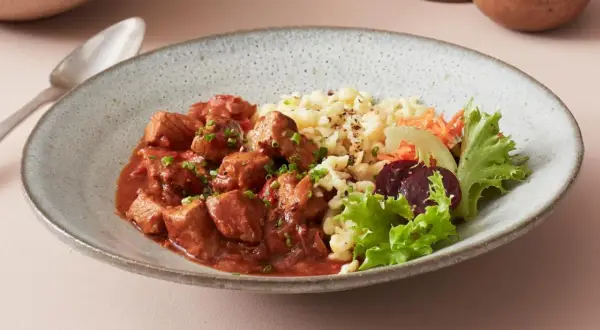 Herzhaftes ungarisches Gulasch mit Nockerln als Beilage, garniert mit frischem Salat und Rote Bete.