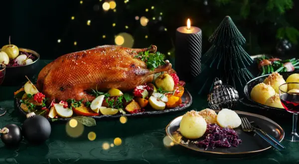 Festliches weihnachtsessen einen tag vorher vorbereiten: goldbraune Gans mit Früchten, Klößen und Rotkohl, Kerzenlicht und Weihnachtsdeko.