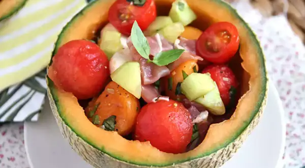 Erfrischender **Salat mit Melone**, Tomaten und Schinken, serviert in einer ausgehöhlten Honigmelone. Ein leichter Genuss!