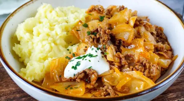 Herzhaftes Schmorkohl mit Hackfleisch, garniert mit einem Klecks Sour Cream und Petersilie, serviert mit cremigem Kartoffelpüree.