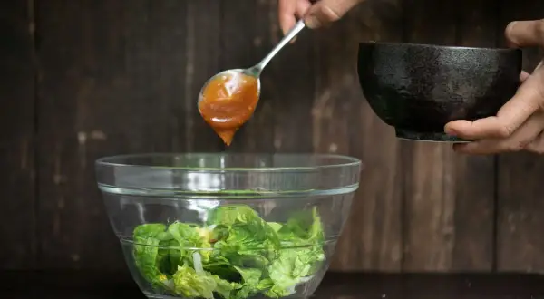 Ein Löffel mit köstlichem Salatdressing, wie im Restaurant, tropft auf frischen Salat in einer Glasschüssel.