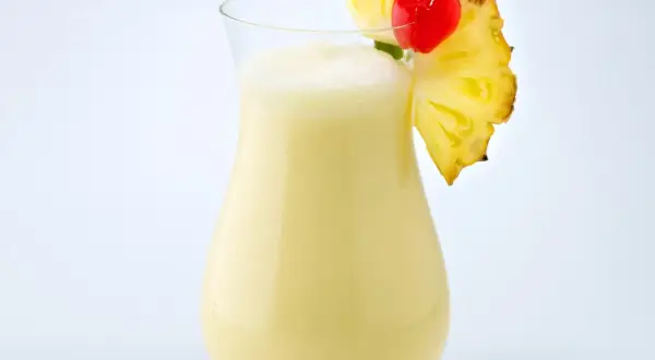 Cremiger Pina Colada mit Ananasstück und Kirsche garniert.