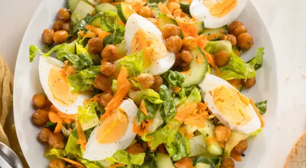 Ein bunter gemischter Salat mit knackigem Salat, Gurkenscheiben, geraspelten Karotten, Kichererbsen und gekochten Eiern.