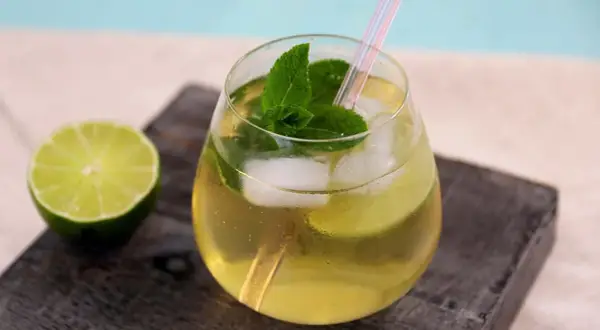 Erfrischender alkoholfreier Hugo mit Minze, Limette und Eiswürfeln, serviert in einem Glas mit Strohhalm.
