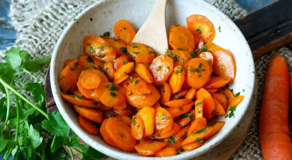 Schmackhafte Karotten-Rezepte: Glasierte Karotten mit Petersilie in einer Schüssel, daneben frische Karotten.