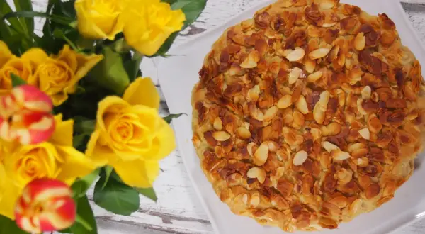 Bienenstich mandelkruste ohne backen, verziert mit gerösteten Mandelsplittern. Daneben ein Strauß gelber Rosen und Tulpen.