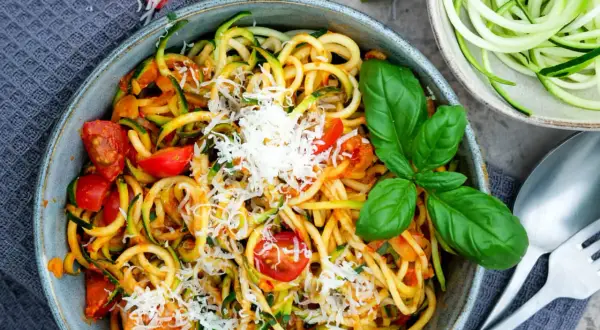 Herzhafte Zucchini-Nudeln mit Tomaten und Parmesan, garniert mit frischem Basilikum. Ein leichtes Gericht, das schmeckt.