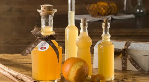 Flaschen mit selbstgemachtem Schnaps, Orangen, Zimtstangen und Sternanis auf Holztisch.