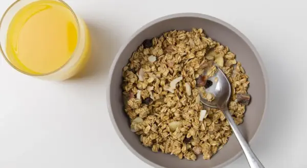 Schüssel mit dinkelflocken oder haferflocken, Nüssen und Trockenfrüchten, daneben ein Glas Orangensaft.