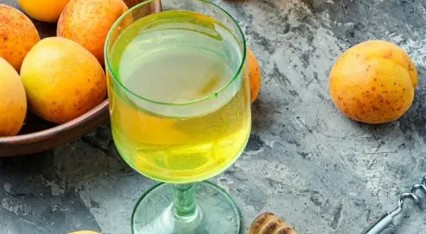 Frische Aprikosen und ein Glas goldener Likör – die Zutaten, um Mirabellenschnaps selber zu machen.