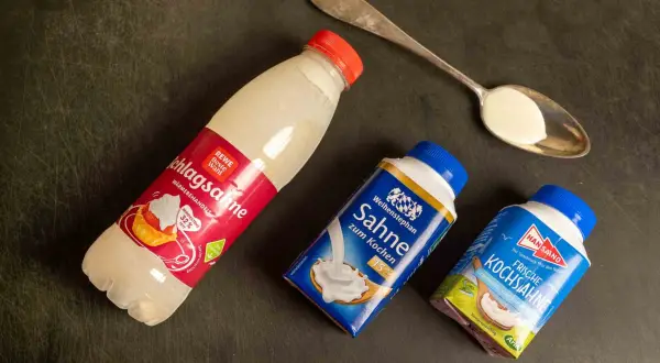 Drei Packungen Sahne zum Backen und Kochen liegen neben einem Löffel mit Sahne.