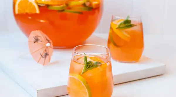 Erfrischende Aperol Bowle mit Orangen- und Limettenscheiben, garniert mit Minze. Perfekt für heiße Sommertage.