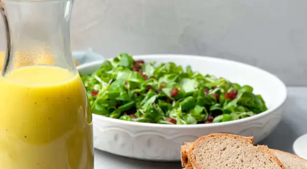 Ein Glas mit gelbem Dressing steht neben einem Salat und Brot. Perfekt für ein Kartoffel Dressing!