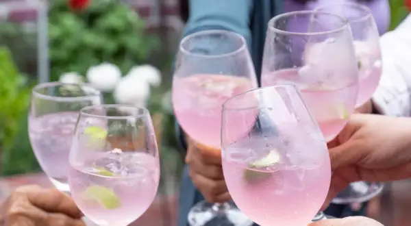 Fünf Gläser mit pinkfarbenem Sarti Spritz, garniert mit Limette, stoßen an.