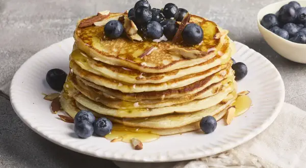 Stapel protein pancakes mit Magerquark, garniert mit Blaubeeren und Mandelsplittern, beträufelt mit Honig.