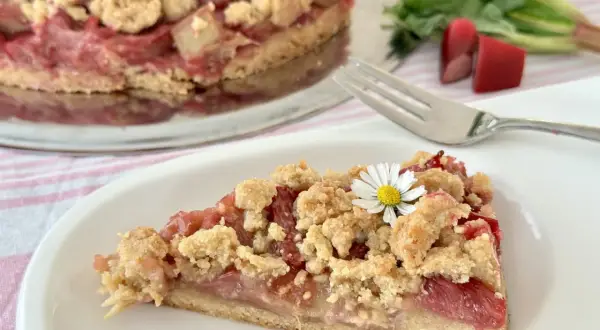 Ein saftiges Stück Rhabarberkuchen mit Schmand und Streuseln, garniert mit einer kleinen Gänseblümchen.