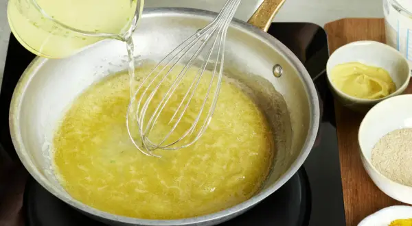 Flüssigkeit wird in eine Pfanne gegossen, während mit einem Schneebesen gerührt wird. Zutaten für eine vegane Sauce Hollandaise werden vorbereitet.