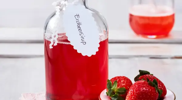 Flasche mit selbstgemachtem Erdbeersirup, garniert mit frischen Erdbeeren. Perfekt für Cocktails oder als Topping.