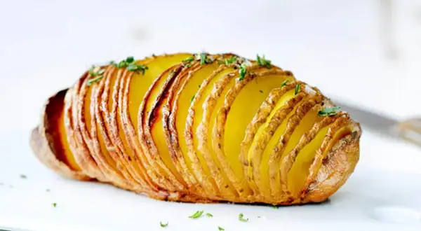 Eine goldbraune Hasselback Kartoffel, knusprig und mit frischen Kräutern bestreut, wartet darauf, genossen zu werden.