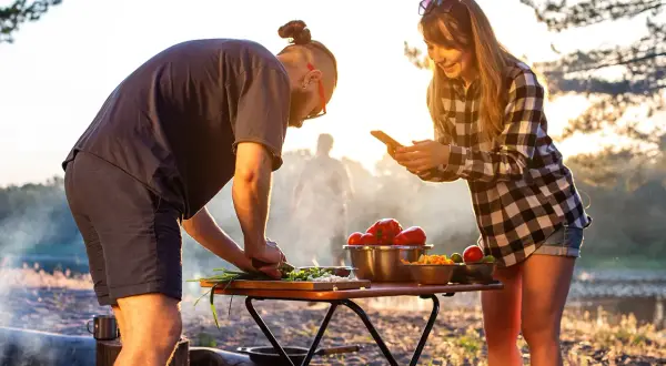 Ein Paar bereitet draußen Gemüse zu, während die Sonne untergeht. Sie kochen im Wohnmobil und genießen die Natur.