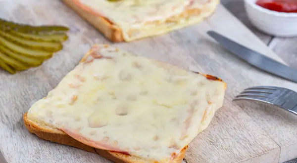 Zwei überbackene Scheiben Brot mit Schinken und Käse, garniert mit Gewürzgurken. Eine Karlsbader Schnitte, perfekt für einen herzhaften Snack.