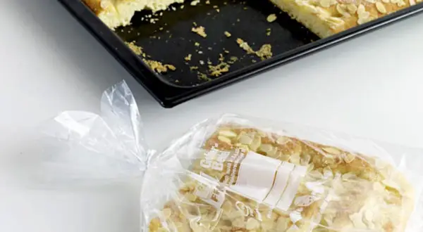 Ein Stück Mandelkuchen ist in einer Plastiktüte verpackt, bereit zum Kuchen einfrieren. Daneben liegt die Backform mit den restlichen Stücken.