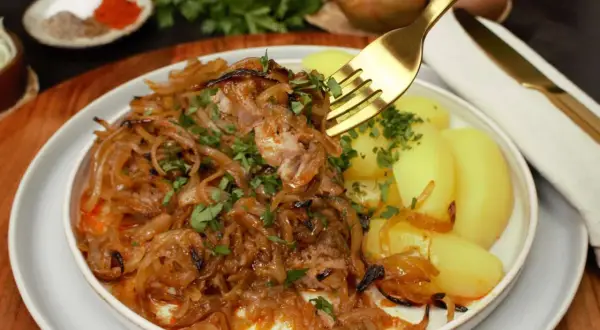Zwiebelfleisch nach Omas Art: Zartes Fleisch mit karamellisierten Zwiebeln und Salzkartoffeln, garniert mit Petersilie. Ein Klassiker, der immer schmeckt.