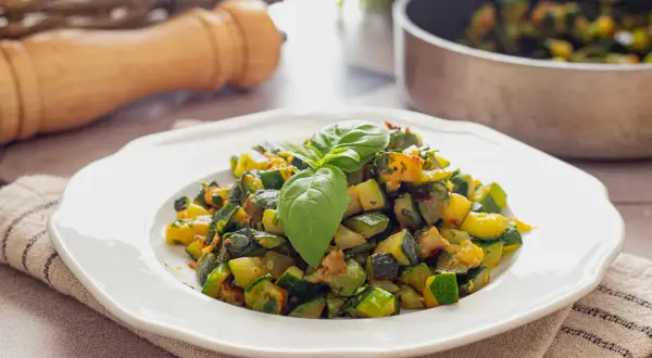 Herzhafte zucchini pfanne, frisch zubereitet und mit Basilikum garniert, serviert auf einem weißen Teller.