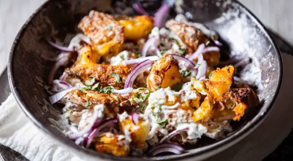 Knuspriger Kartoffelsalat mit cremiger Soße, roten Zwiebeln und frischer Petersilie in einer dunklen Schüssel.