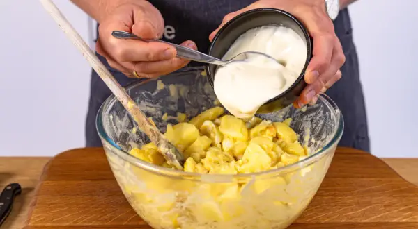 Hände geben Mayonnaise zu Kartoffeln für norddeutschen Kartoffelsalat.