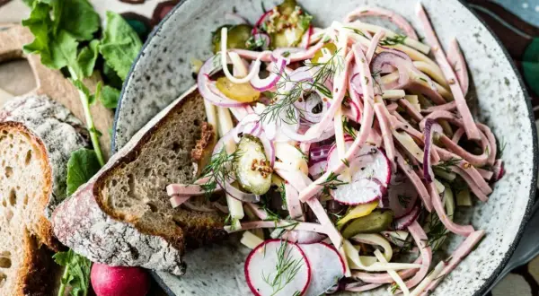 Ein bayerischer Wurstsalat, garniert mit Radieschen, Zwiebeln und Dill, serviert mit Bauernbrot.