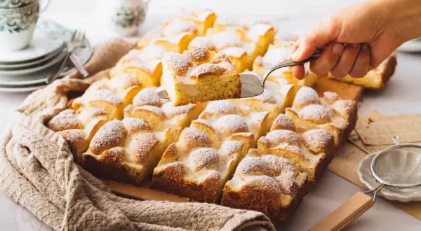 Ein Stück eines saftigen Blechkuchens mit Puderzucker wird herausgehoben. Perfekt für schnelle Blechkuchen Rezepte.