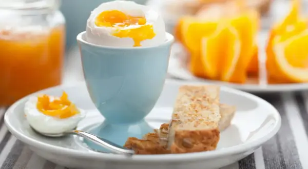 Ein perfekt gekochtes Ei im Wasserkocher, serviert mit Toast und Orangenspalten.