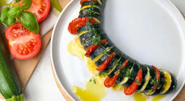 Zucchini Caprese: geschichtete Zucchini, Tomaten und Kräuter, beträufelt mit Olivenöl auf einem weißen Teller.