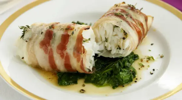 Zwei Fischröllchen, in Speck gewickelt, auf Spinatbett. Ein festliches Gericht, perfekt für Fischgerichte an Weihnachten.