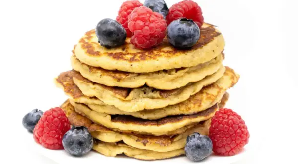 Stapel zuckerfreier Bananen-Pancakes, garniert mit frischen Himbeeren und Blaubeeren. Ein gesunder Genuss!