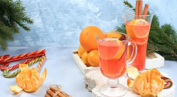 Zwei Gläser mit einem heißen Aperol-Getränk, garniert mit Orangen und Zimt. Daneben Mandarinen, Zuckerstangen und Tannenzweige.