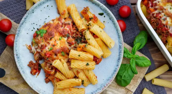 Herzhaftes Bolognese Gratin mit Rigatoni, überbacken mit geschmolzenem Käse, garniert mit frischem Basilikum und Tomaten.