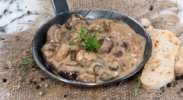 Herzhafte Champignon Rahmsauce in einer Pfanne, garniert mit Rosmarin, serviert mit knusprigem Brot.