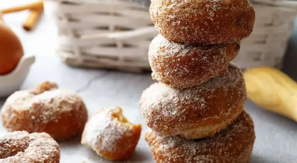 Gestapelte, zuckerglasierte Apfelkrapfen aus dem Airfryer, daneben weitere Krapfen und ein Ei.