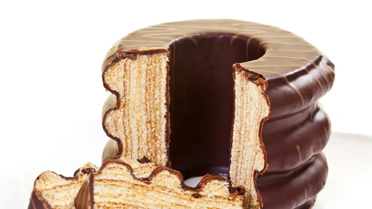 Ein angeschnittener Baumkuchen mit Schokoladenglasur, dessen Schichten die aufwendige Baumkuchen Herstellung zeigen.