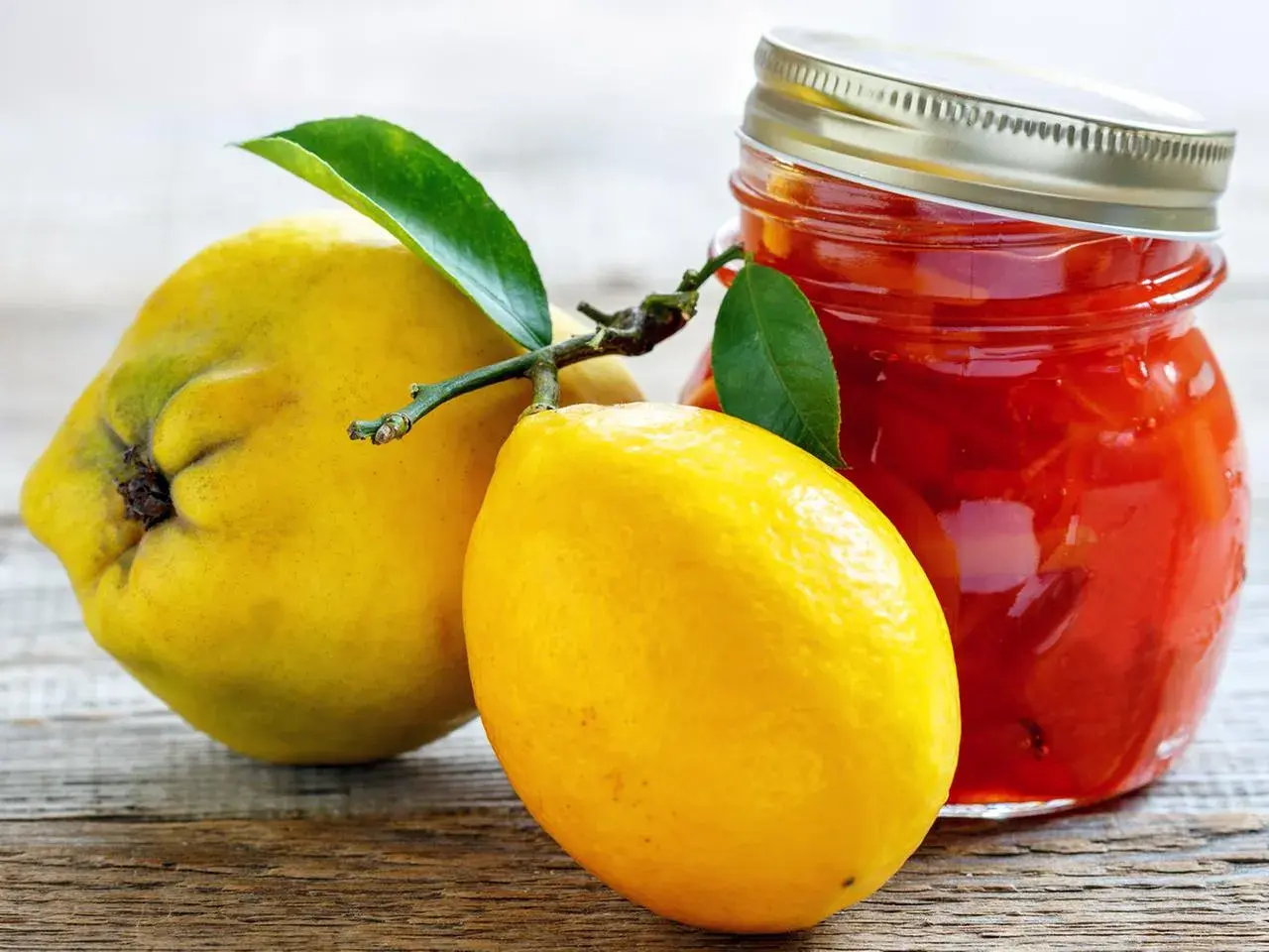 Gelbe Quittenfrucht und Zitrone neben einem Glas mit roter Marmelade.