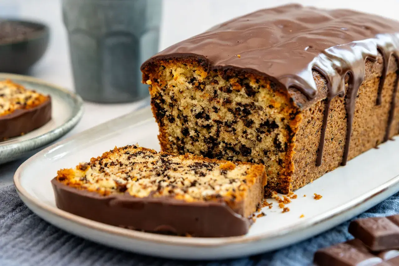 Ein saftiger Stracciatella Kuchen mit Schokoladenglasur, ein Stück davon auf einem Teller, daneben ein ganzer Kuchen.