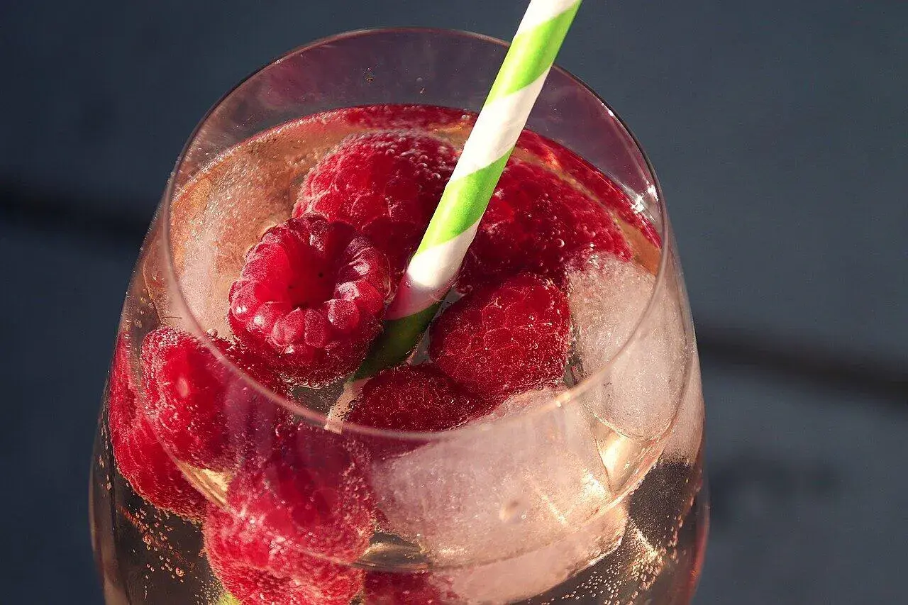 Erfrischender Pfirsich Spritz mit Himbeeren und Eiswürfeln in einem Glas, bereit zum Genießen.