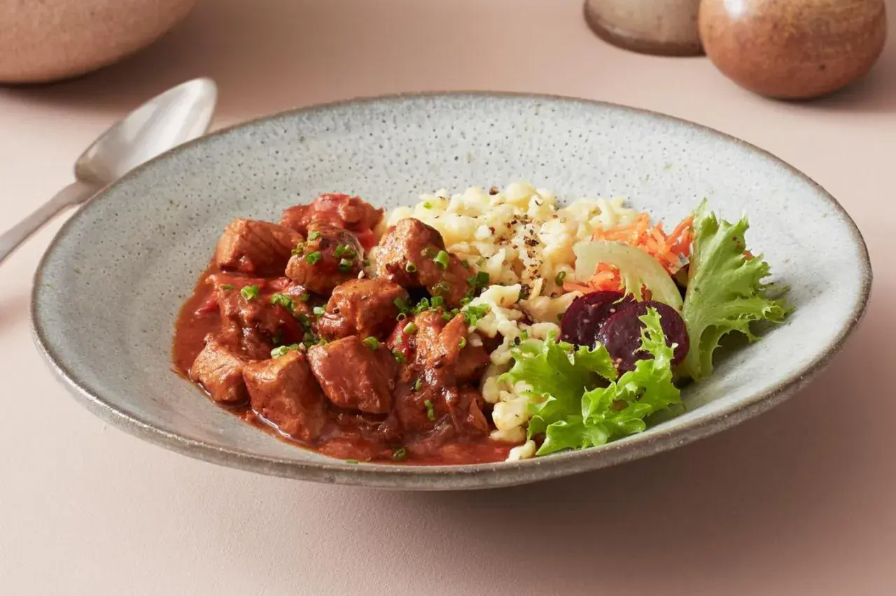 Herzhaftes ungarisches Gulasch mit Nockerln als Beilage, garniert mit frischem Salat und Rote Bete.