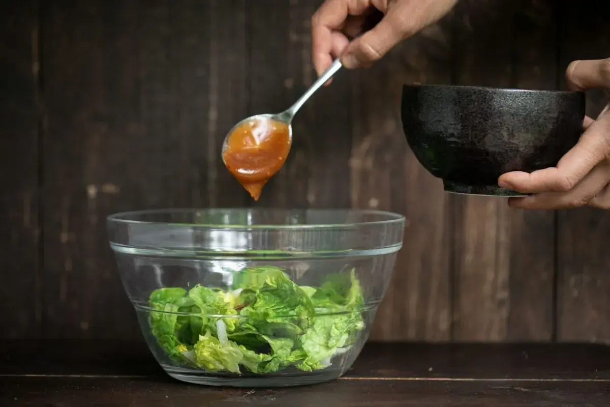 Ein Löffel mit köstlichem Salatdressing, wie im Restaurant, tropft auf frischen Salat in einer Glasschüssel.