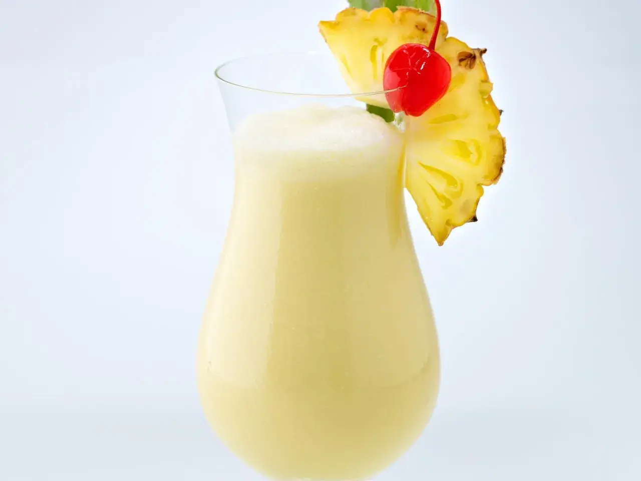 Cremiger Pina Colada mit Ananasstück und Kirsche garniert.