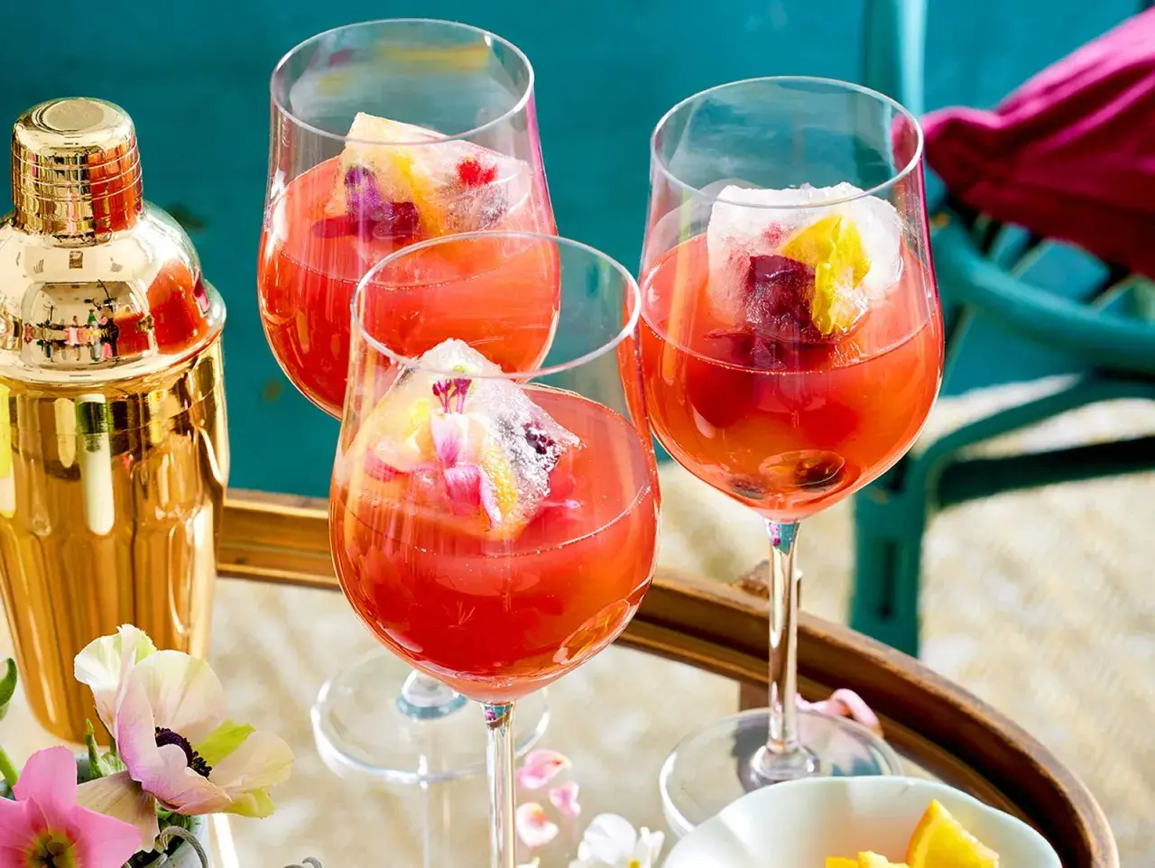 Erfrischendes Aperol Spritz Rezept: Drei Gläser mit leuchtend rotem Aperol, Eiswürfeln und Fruchtgarnitur. Ein goldener Shaker steht bereit.